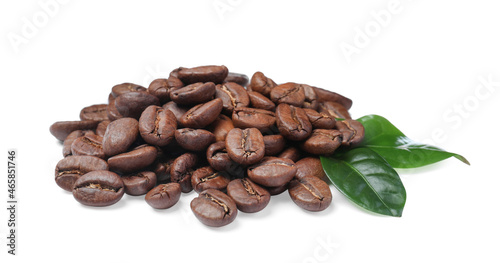 Pile of roasted coffee beans with fresh leaves on white background