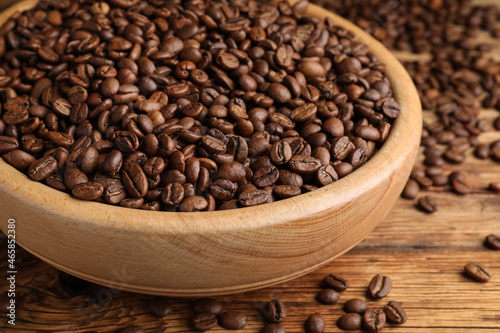 Bowl of roasted coffee beans on wooden table, closeup