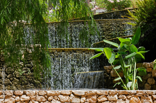 Fototapeta Naklejka Na Ścianę i Meble -  Artificial waterfall in a park among plants and tree branches