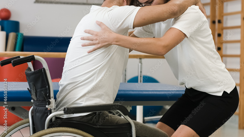 Person with disability and female physiotherapist, exercise standing up and proper lifting technique from a wheelchair. Person with disability and female physiotherapist, exercise standing up and proper lifting technique from a wheelchair.
