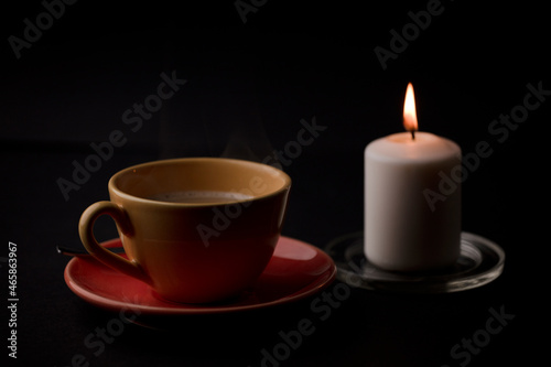 cup of tea with hot smoke and lit candle. on the desk at home, power outage (focus on cup).