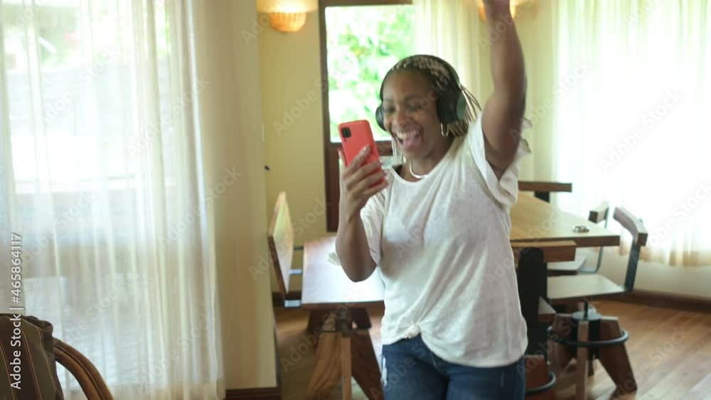 Mujer afroamericana bailando mientras escucha música con el celular conectado a los audífonos en su casa