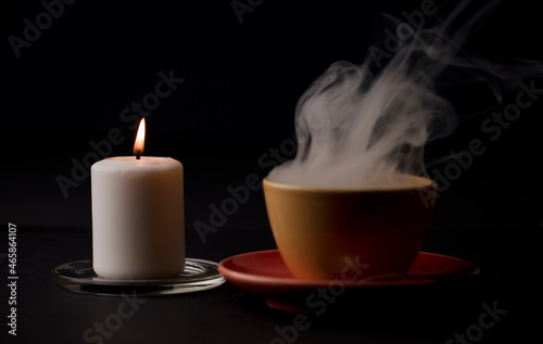cup of tea with hot smoke and lit candle. on the desk at home, power outage (focus on lit candle).