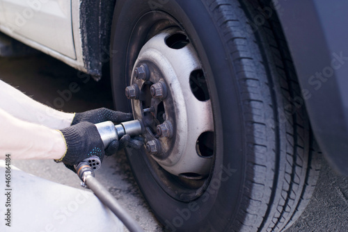 A mechanic at a service station replaces a car wheel, a worker's hands in black fuel oil and a tool for unscrewing bolts close-up near the wheel. Tire service, workflow