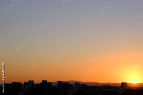 都市の夜明け、早朝ビルの隙間から太陽が昇り辺りはオレンジ色に染まる。ビルはシルエットに浮かぶ