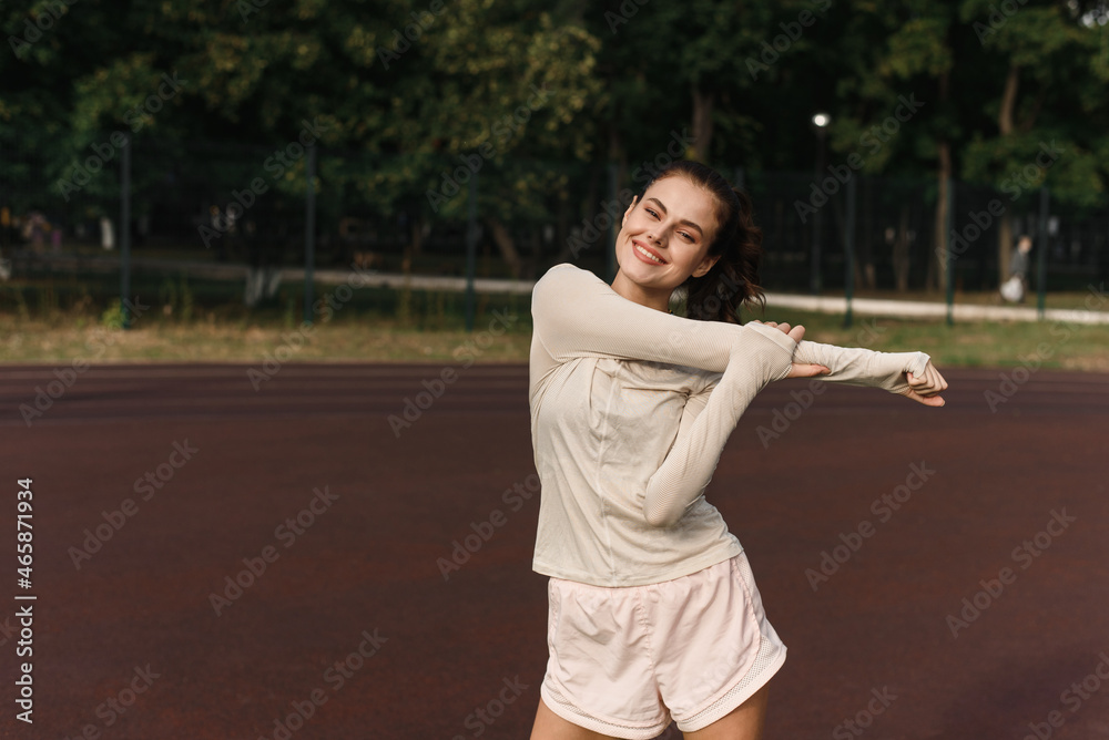 Young woman stretches her arms while playing sports in the stadium Young woman stretches her arms while playing sports in the stadium