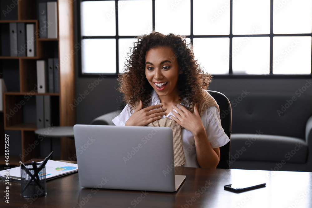 Beautiful African-American woman with laptop video chatting in office at night