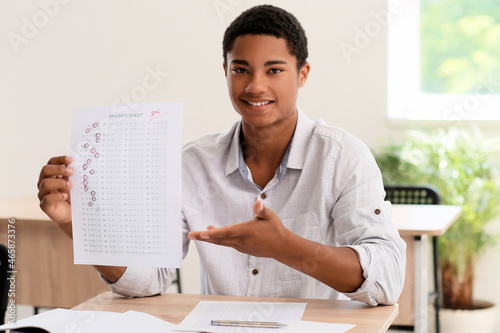 Happy African-American student with answer sheet for school test in classroom