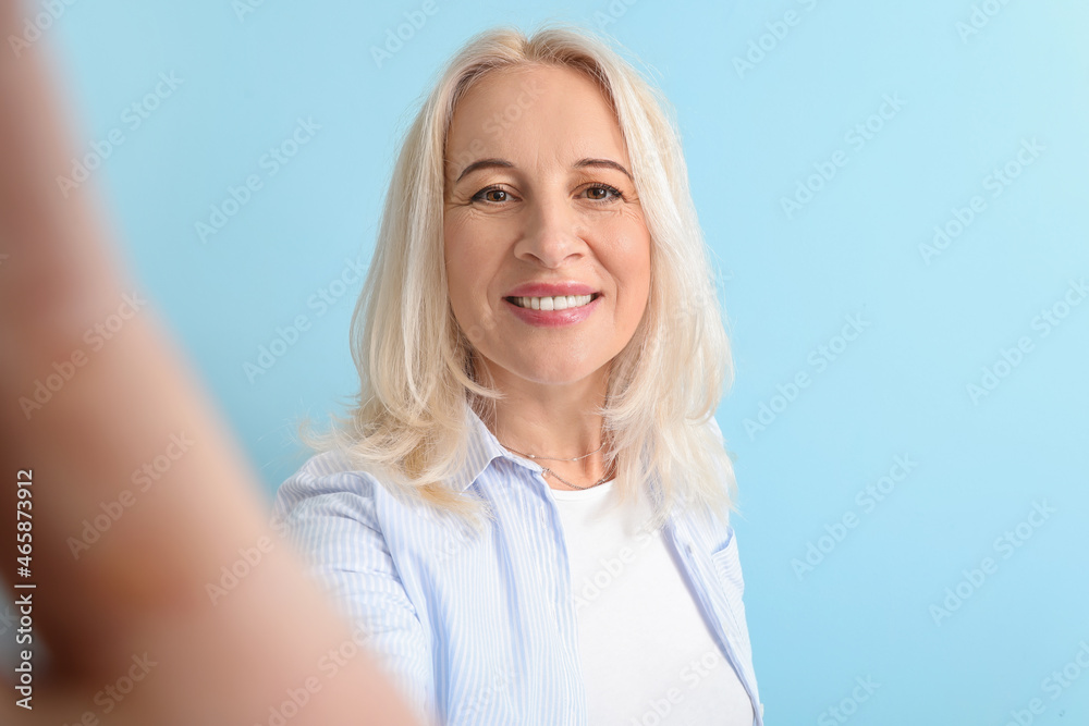 Beautiful mature woman taking selfie on blue background Beautiful mature woman taking selfie on blue background