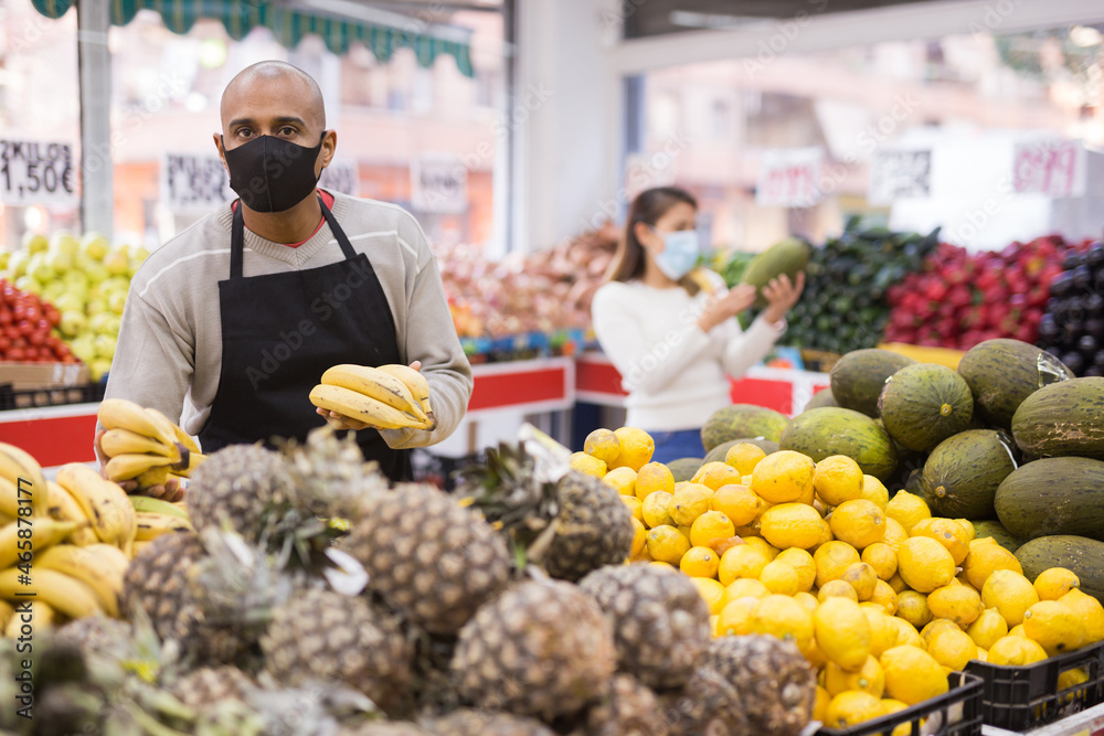 Friendly grocery store in protective mask employee lays ripe bananas on the counter