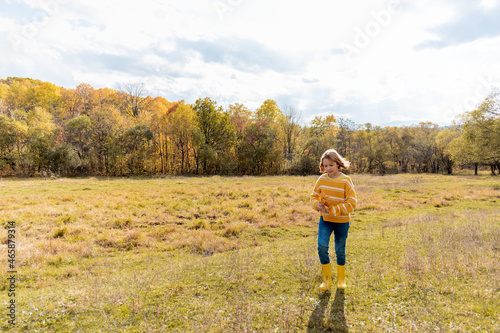 Girl preteen in knitted sweater runs in yellow rubber boots in the meadow. Cozy slow lifestyle concept.