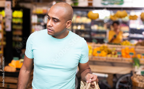 Portrait of focused Hispanic man choosing food products on shelves in grocery shop