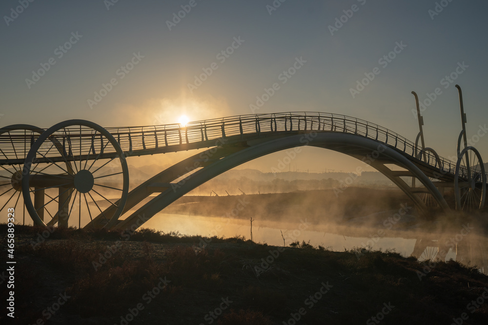 Bicycle-shaped bridge with water fog rising from the beach Bicycle-shaped bridge with water fog rising from the beach