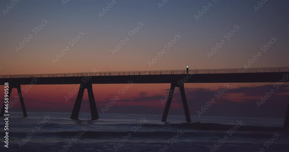 Person walking on sea bridge after sunset and shinning towards camera Person walking on sea bridge after sunset and shinning towards camera
