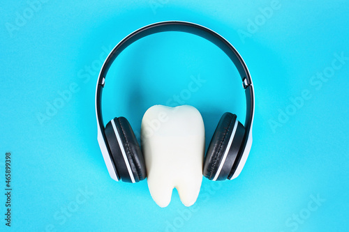 Tooth in white wireless headphones on a blue background. Teeth listening concept.