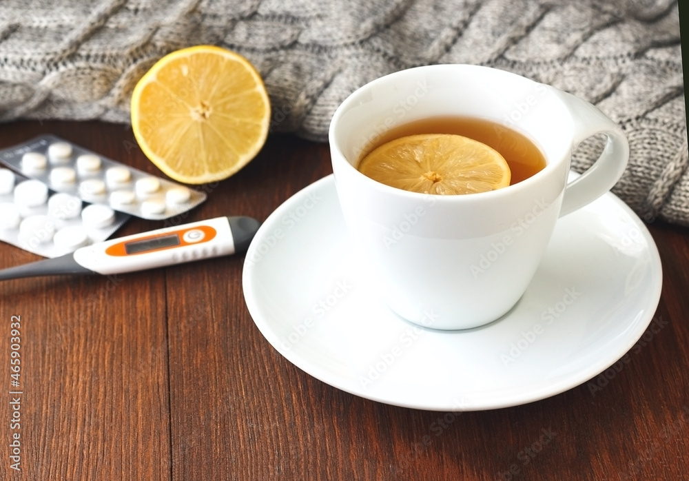 Pills, thermometer, white cup of hot tea with lemon for colds on wooden background Pills, thermometer, white cup of hot tea with lemon for colds on wooden background