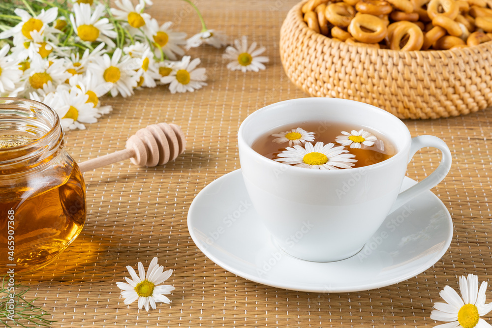 Herbal tea with chamomile flowers in cup and honey on rattan matting Herbal tea with chamomile flowers in cup and honey on rattan matting