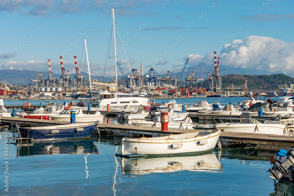 Large port with many boats moored, cranes and container ships. International harbor in the Gulf of La Spezia on a sunny winter day. Liguria, Italy, Europe.