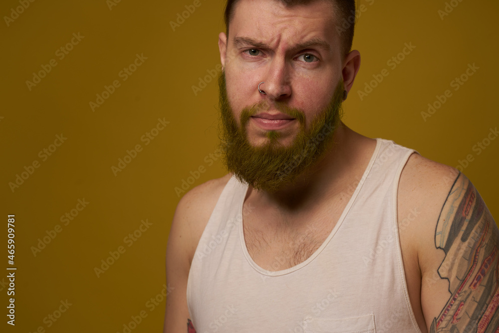 a bearded man with a serious expression in a white t-shirt with tattoos on his arms
