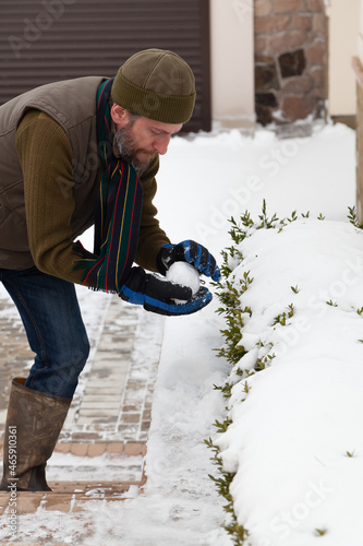 Man with beard sculpts snowball in yard