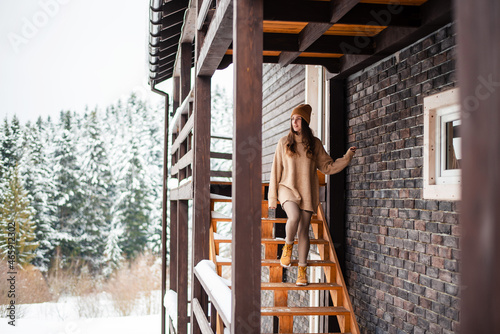 Woman on stairs of wooden house enjoying snowy forest