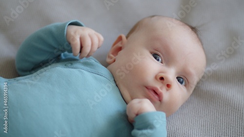 Cute two-month-old baby in blue clothes looks into camera. Sweet newborn boy lies on the sofa. Shooting from the upper angle of a chubby male kid. Beautiful infant boy with blue eyes.