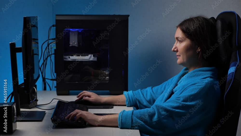 Young brunette long-hired woman plays videogame tensely on large computer screen sitting in gaming chair in semi-dark room illuminated by monitor. Young brunette long-hired woman plays videogame tensely on large computer screen sitting in gaming chair in semi-dark room illuminated by monitor.
