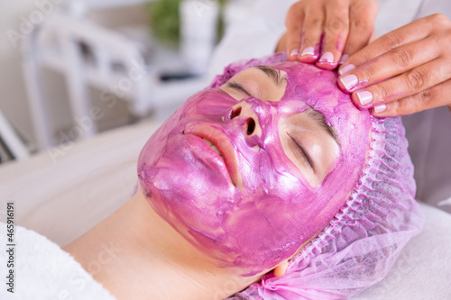 Cosmetologist making  massage the skin of the forehead. Woman in a spa salon on cosmetic procedures for facial care. Beautician applies a woman a therapeutic cream on her face. .
