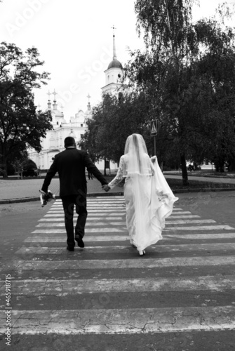 The bride and groom on a pedestrian crossing in the city from the back. Wedding couple crossing the road black and white photo. High quality photo