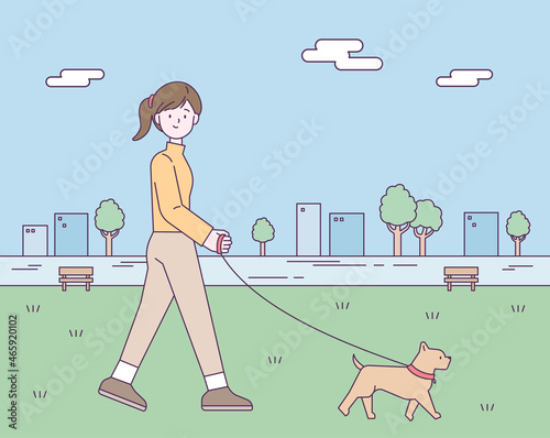 A woman is taking a walk in a park in the city center with her dog. flat design style vector illustration.