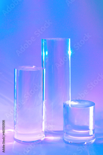Abstract surreal scene - empty stage with three clear glass cylinder podiums on pastel holographic neon colored background. Pedestal for cosmetic product packaging mockups display presentation