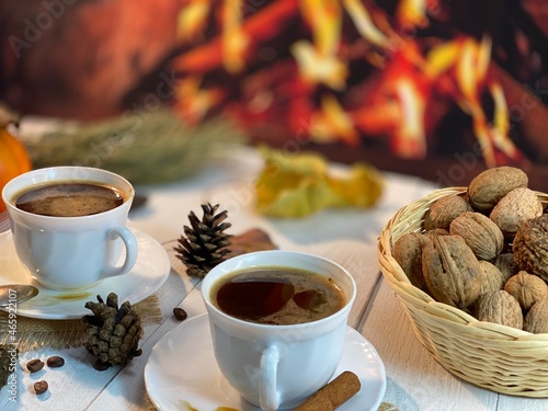 On the wooden table by the fireplace are white cups with coffee and a basket of nuts