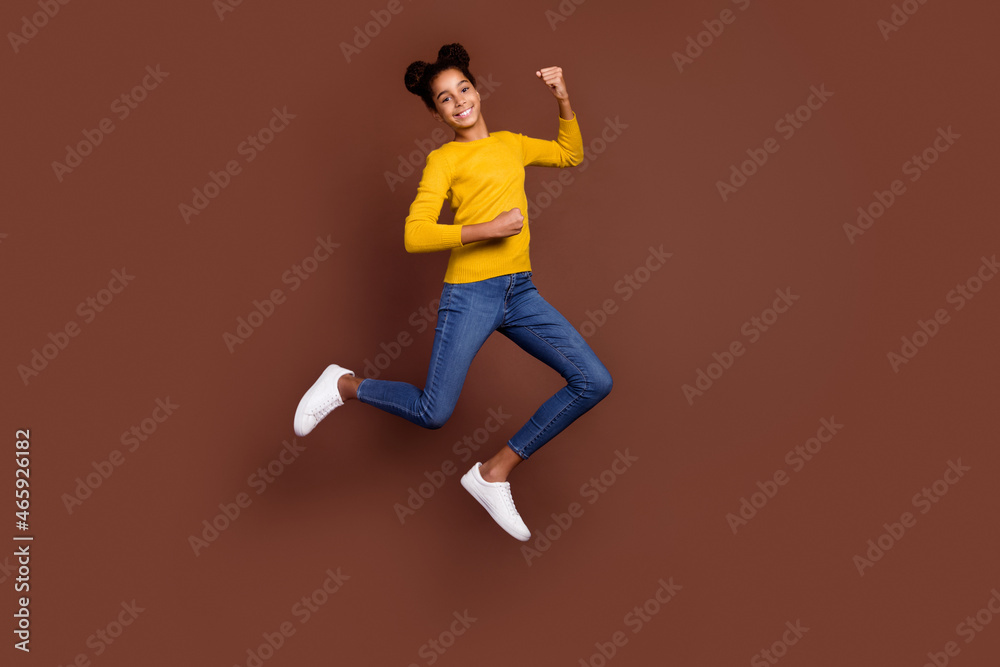 Full size photo of style small girl jump wear shirt jeans sneakers isolated on brown color background Full size photo of style small girl jump wear shirt jeans sneakers isolated on brown color background
