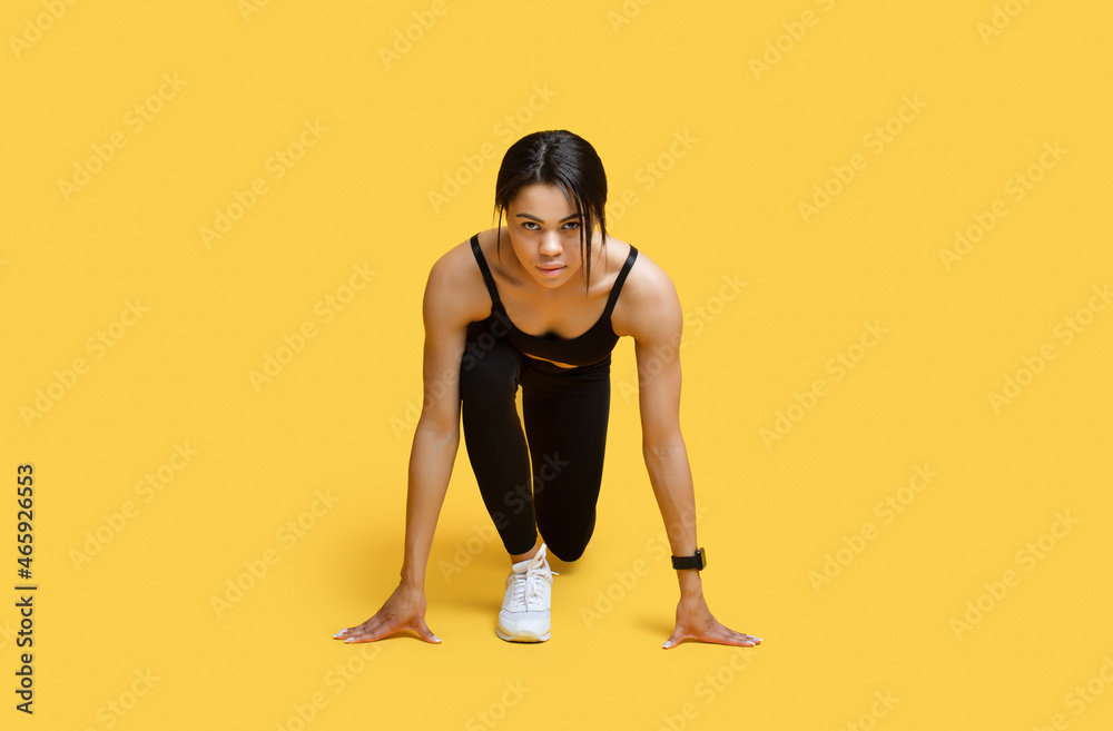 Sprint concept. Young african american female athlete in starting position ready for running, yellow background - obrazy, fototapety, plakaty 