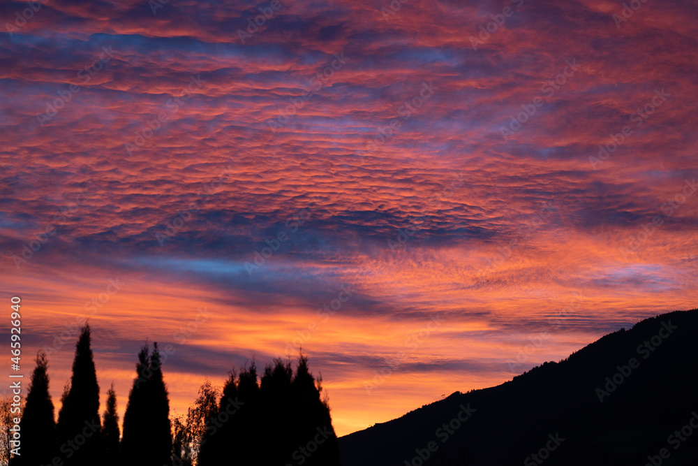 a breathtaking sunrise with a colorful pink, orange, blue sky and mountain- and tree silhouttes