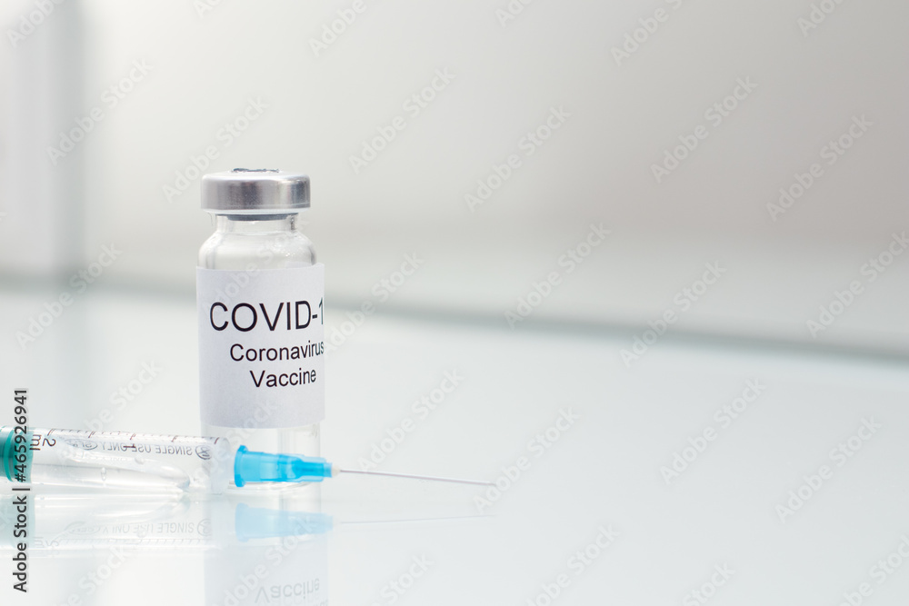 COVID 19 Vial with coronavirus vaccine and syringe on white glass table
