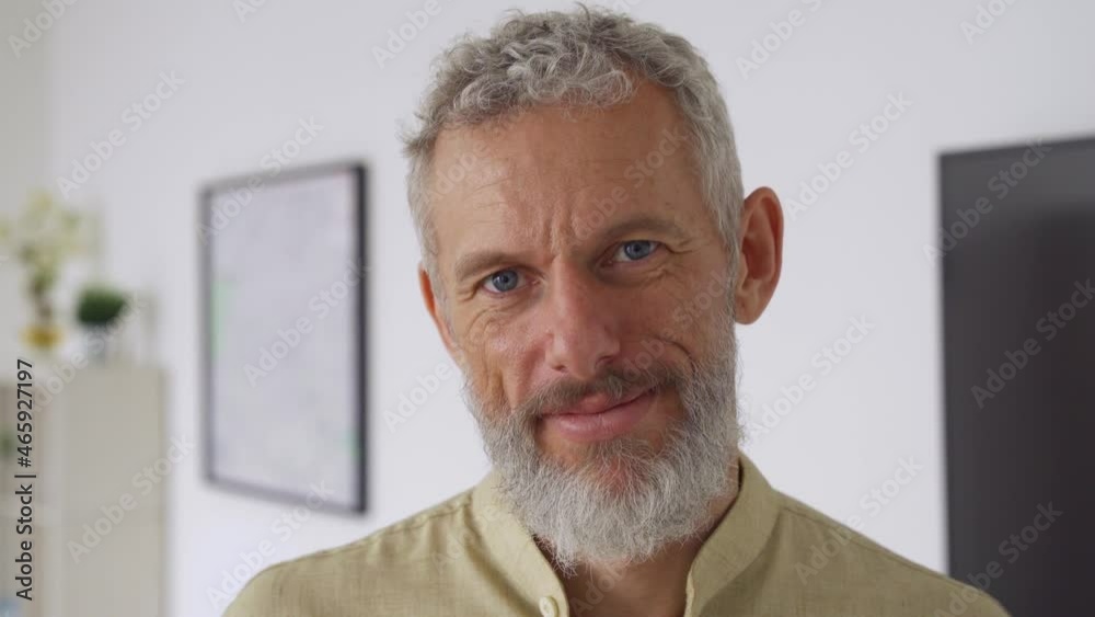 Calm smiling relaxed mature older bearded hipster man looking at camera. Close up portrait of happy handsome confident middle aged 50s male professional, standing at home office posing indoors.