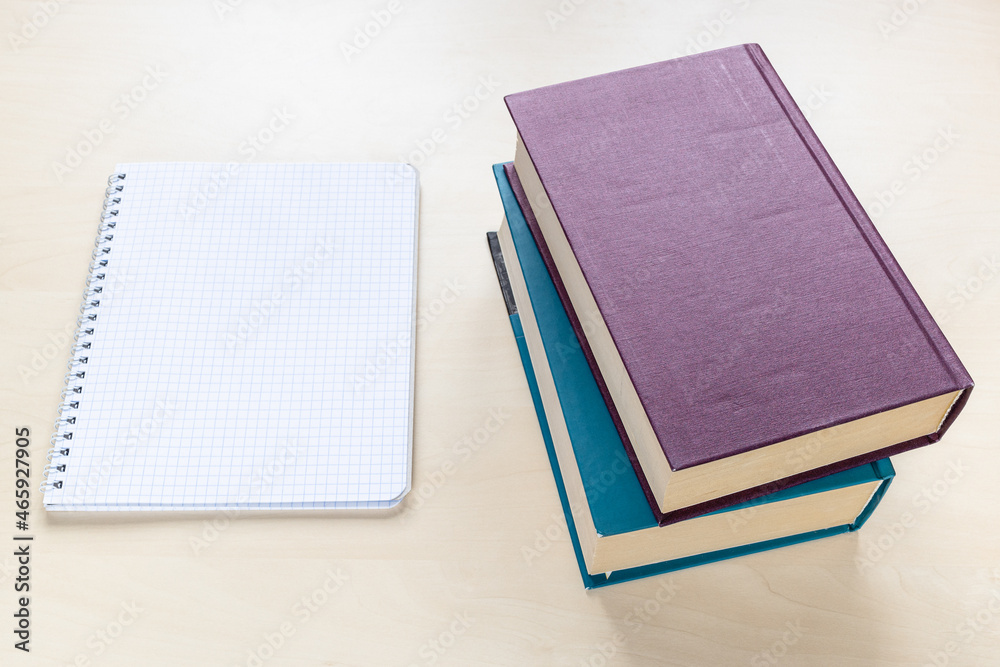 above view of two thick books and blank spiral notebook with squared paper on light brown wooden board above view of two thick books and blank spiral notebook with squared paper on light brown wooden board