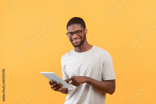 Modern work and online communication. Happy african american guy in glasses typing in digital tablet