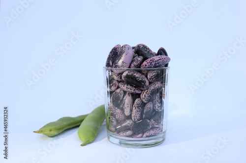 The green hulls and fresh harvested beans of Scarlet runner beans in a glass on a white background.