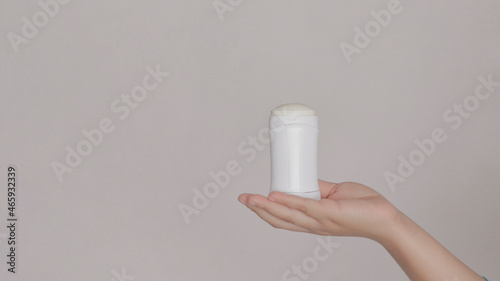 Hand showing a white stick deodorant, on plain background.