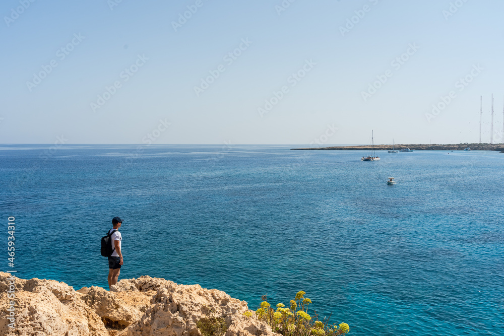 Man traveler standing on rock and looking at blue sea. Wanderlust concept.