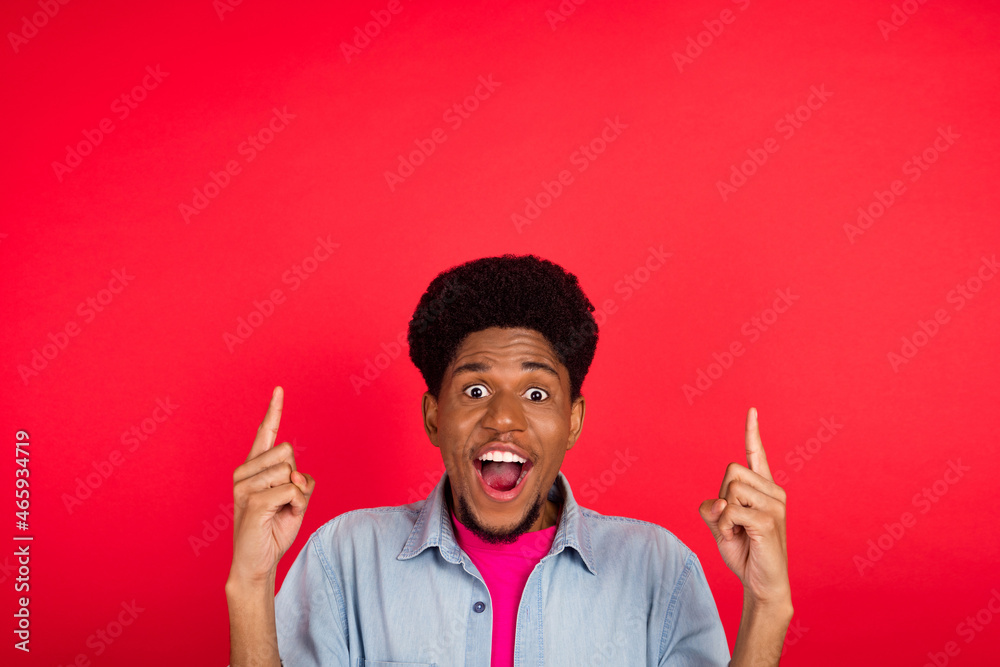 Photo of young afro guy happy positive smile indicate fingers empty space ad promo sale select isolated over red color background Photo of young afro guy happy positive smile indicate fingers empty space ad promo sale select isolated over red color background