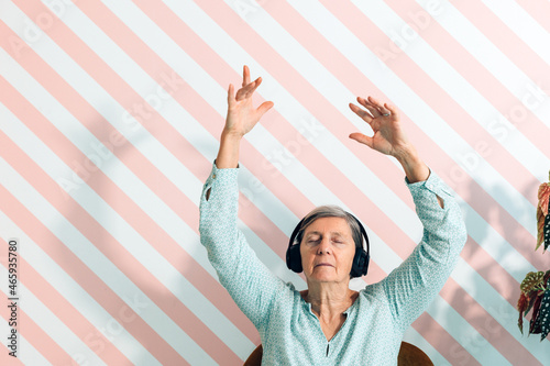 elderly lady in her seventies listens to music with headphones moving her arms in the air and letting herself be carried away by the sound keeping her eyes closed - leisure time photo