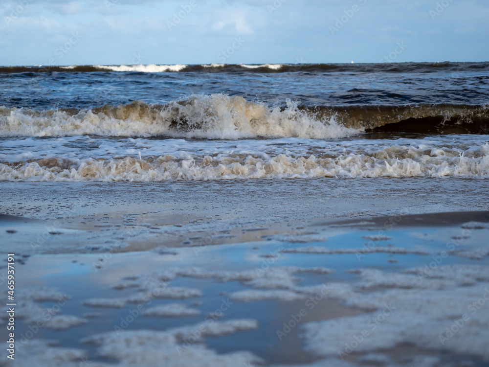 Wave with white foamy coastline beach. Sandy shore.