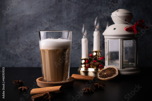 spice coffee with milk and foam, cinnamon sticks on blach background. christmas drink, chai latte. candles and lights photo