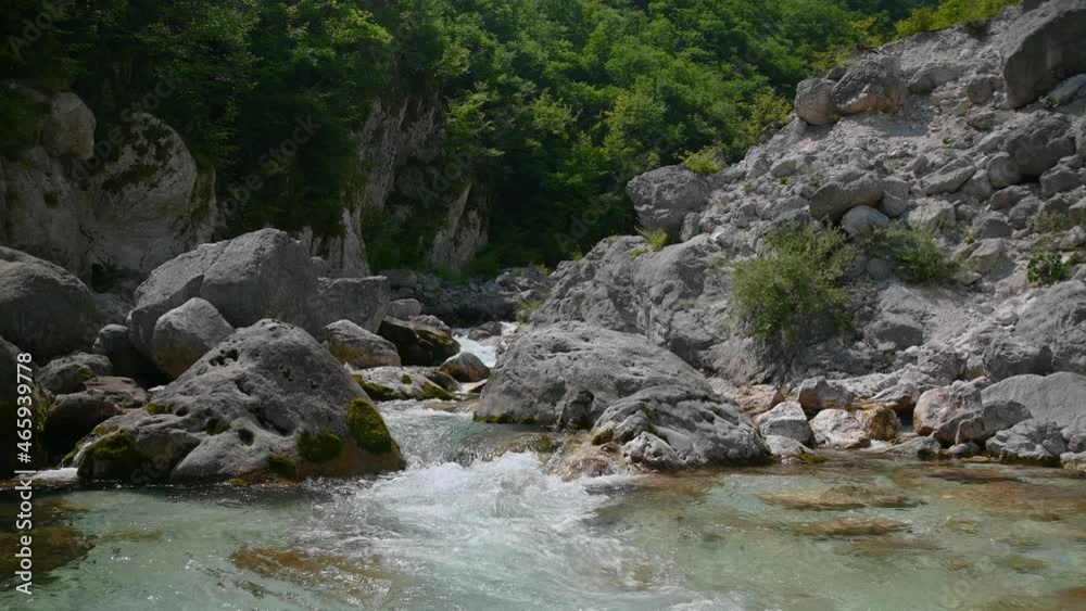 Low angle view of pristine stream flowing in alpine valley. Clear water in clean environment. Ecology concept. Creek flowing between huge rocks. Bright summer day. Real time, static shot Low angle view of pristine stream flowing in alpine valley. Clear water in clean environment. Ecology concept. Creek flowing between huge rocks. Bright summer day. Real time, static shot