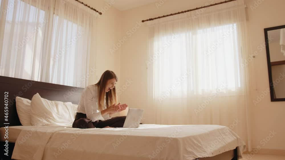 Pretty young woman sitting on bed and gesturing emotionally while looking on computer screen. Happy lady getting some good news. Concept of human expressions and technology. Pretty young woman sitting on bed and gesturing emotionally while looking on computer screen. Happy lady getting some good news. Concept of human expressions and technology.