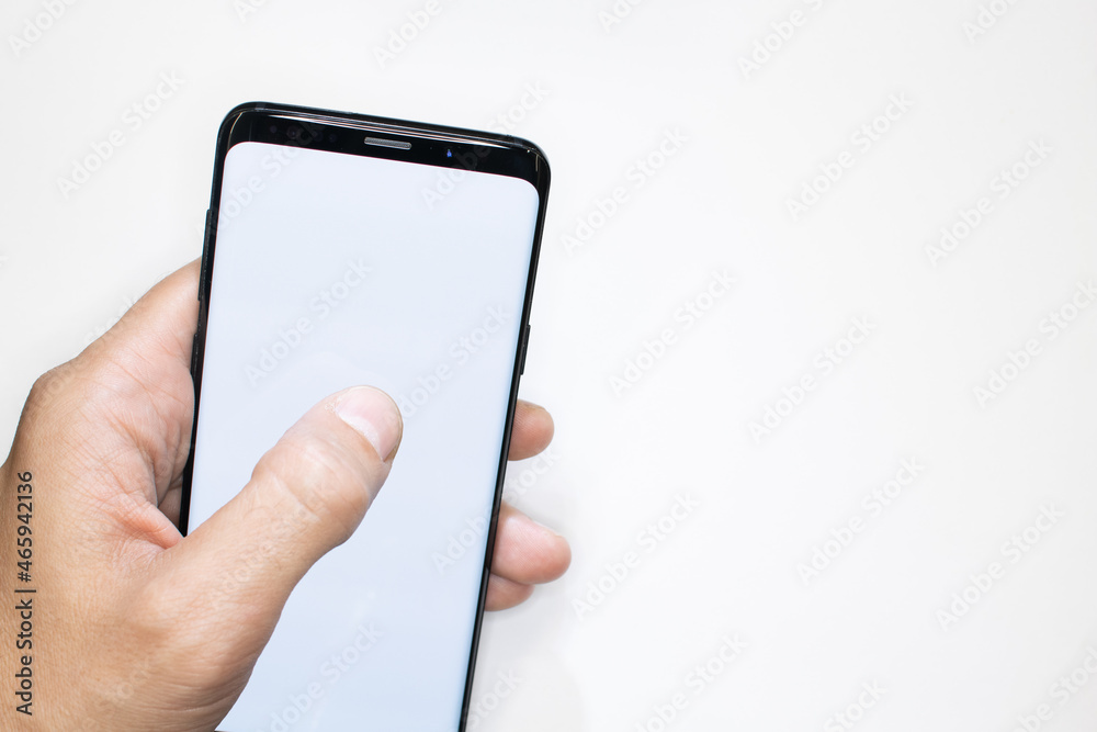 Holding smartphone on white background. Man's hand scrolling smartphone with white screen as template. White background and empty smartphone frame. Thumb finger on telephone screen