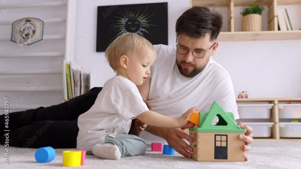 Father and Toddler Son playing with Wooden Toy House, Dad Educating and Stimulating his Child, Playing in Kids Room sitting on the Floor and Bonding, Real Time, Close Up Father and Toddler Son playing with Wooden Toy House, Dad Educating and Stimulating his Child, Playing in Kids Room sitting on the Floor and Bonding, Real Time, Close Up